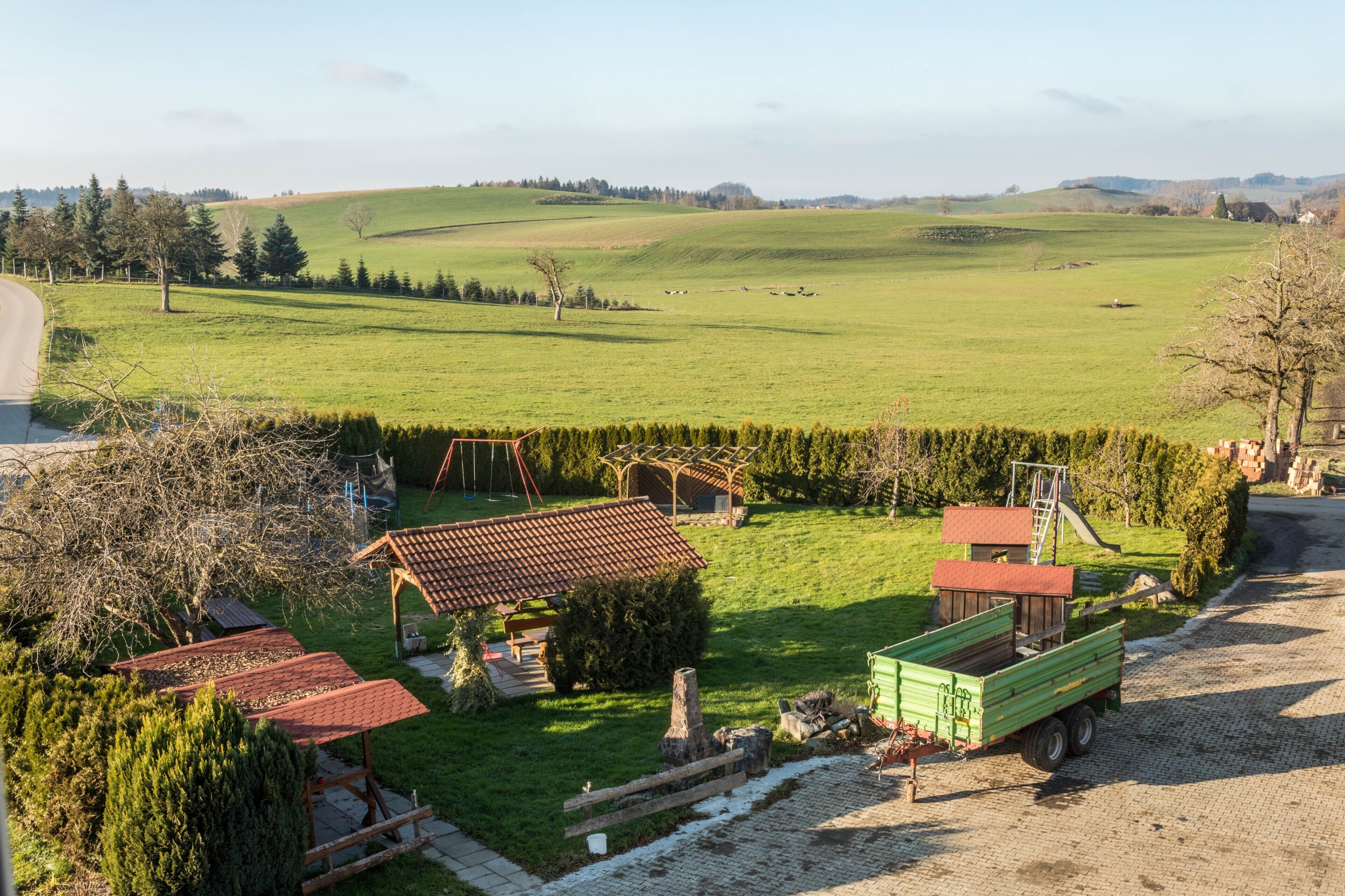 Un paisaje rural con un camión verde, una estructura de madera y una zona cercada.