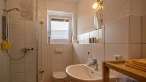 Et badeværelse med bruser, toilet, vask og et vindue.