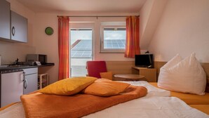 Hotelværelse med seng, skrivebord, stol, fjernsyn, vækkeur og udsigt til solpaneler udenfor.
