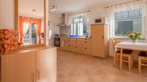 Una cocina con estufa, horno y armarios, una mesa de comedor con sillas y una ventana con cortinas.