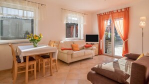 Una sala de estar con un sofá, una televisión, una mesa de comedor con sillas y una ventana con cortinas.