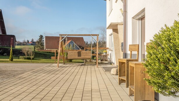 Un espacio al aire libre con un columpio de madera, un banco y una planta en maceta.