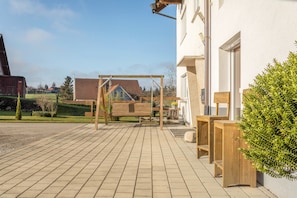 Un espace extérieur aménagé avec une balançoire en bois, un banc et un pot de fleurs.