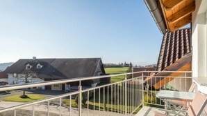 A balcony with a metal railing, a wooden table, and a view of houses and a clear sky. - Cozy Holiday Apartment "Romanshorn" on a Farm near Lake Constance (Neukirch)