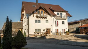 A two-story building with a sloped roof, multiple windows, and a balcony. - Cozy Holiday Apartment "Romanshorn" on a Farm near Lake Constance (Neukirch)