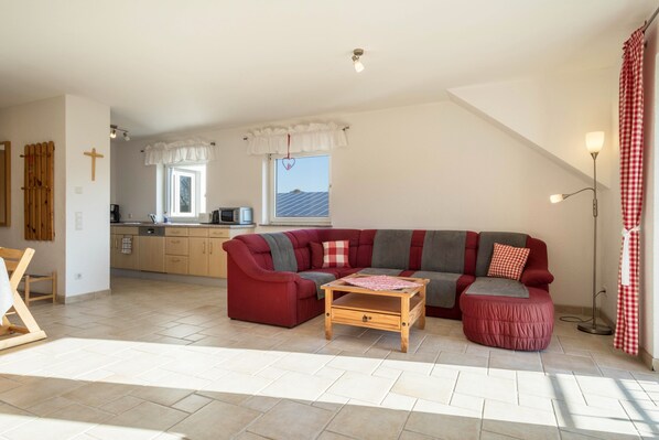 A spacious living area with a red sectional sofa, a wooden coffee table, and a kitchen in the background.