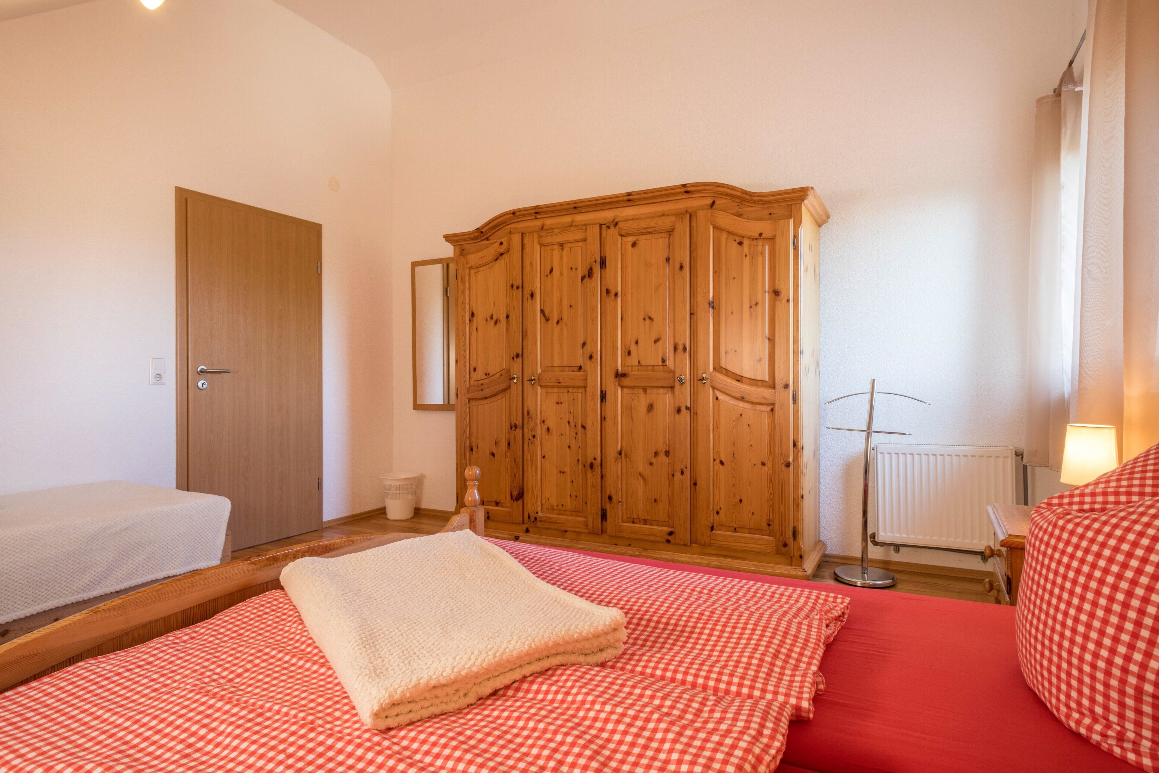 Ein Schlafzimmer mit einem Holzschrank, einem Bett mit rot-karierter Bettwäsche, einem weißen Lattenrost und einer Heizung.