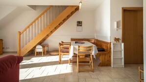 A room with a wooden staircase, a dining table with chairs, a bench, a small white shelf, and a door. - Cozy Holiday Apartment "Romanshorn" on a Farm near Lake Constance (Neukirch)