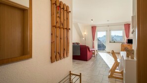 A room with a wooden wall-mounted rack, a red sofa, a small table, and a window with a view. - Cozy Holiday Apartment "Romanshorn" on a Farm near Lake Constance (Neukirch)