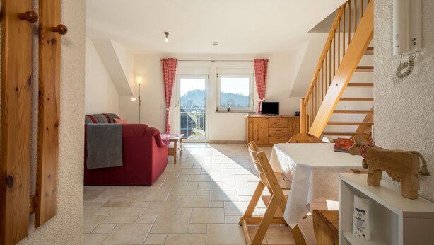 A room with a wooden staircase, a red sofa, a dining table, and a view through a window. - Cozy Holiday Apartment "Romanshorn" on a Farm near Lake Constance (Neukirch)