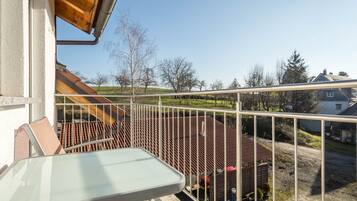 Un balcon doté d’une rambarde en métal, d’une table et offrant une vue sur une maison et des arbres.