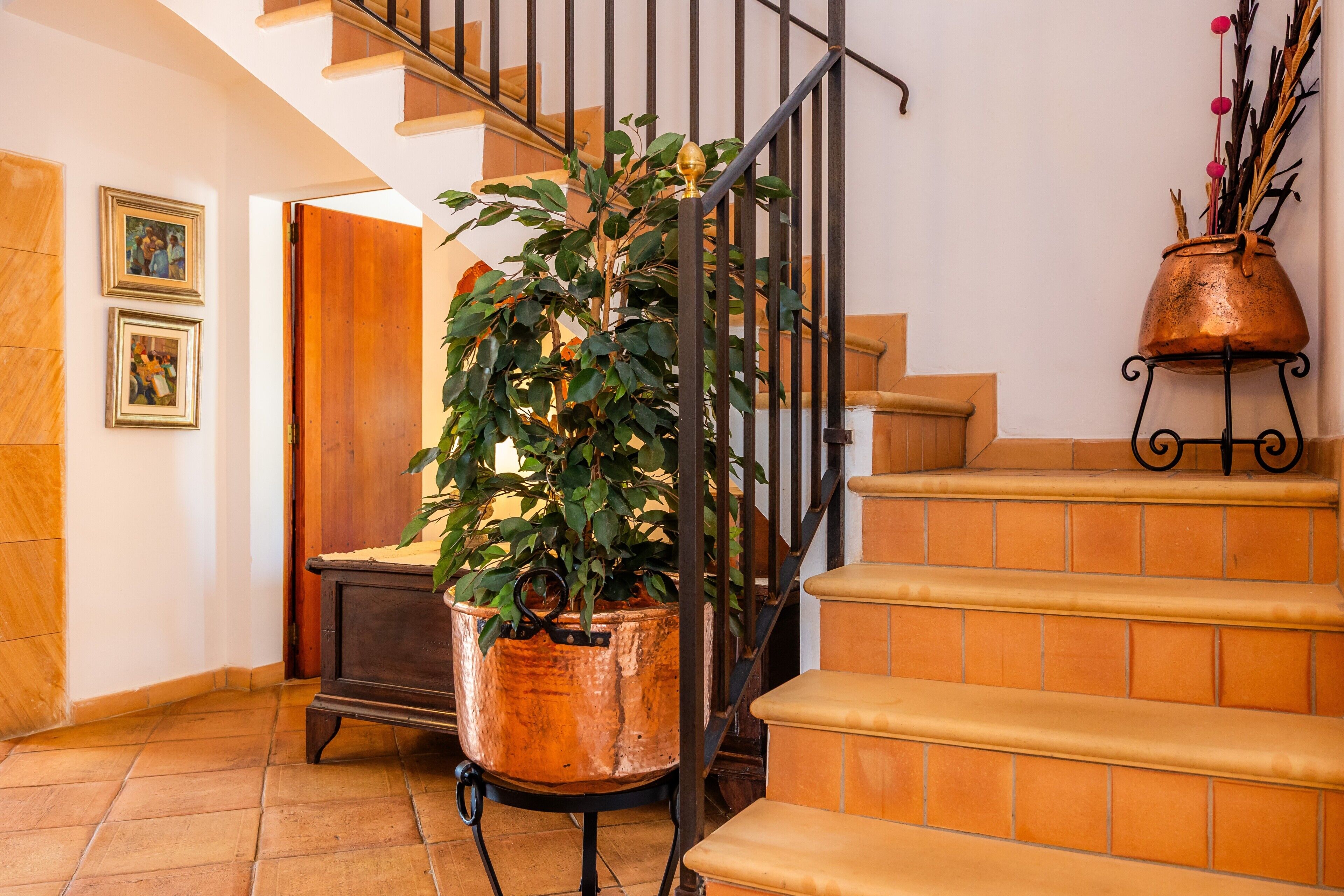 A staircase with a copper pot on the landing, a potted plant on the stairs, and a wooden door in the background.