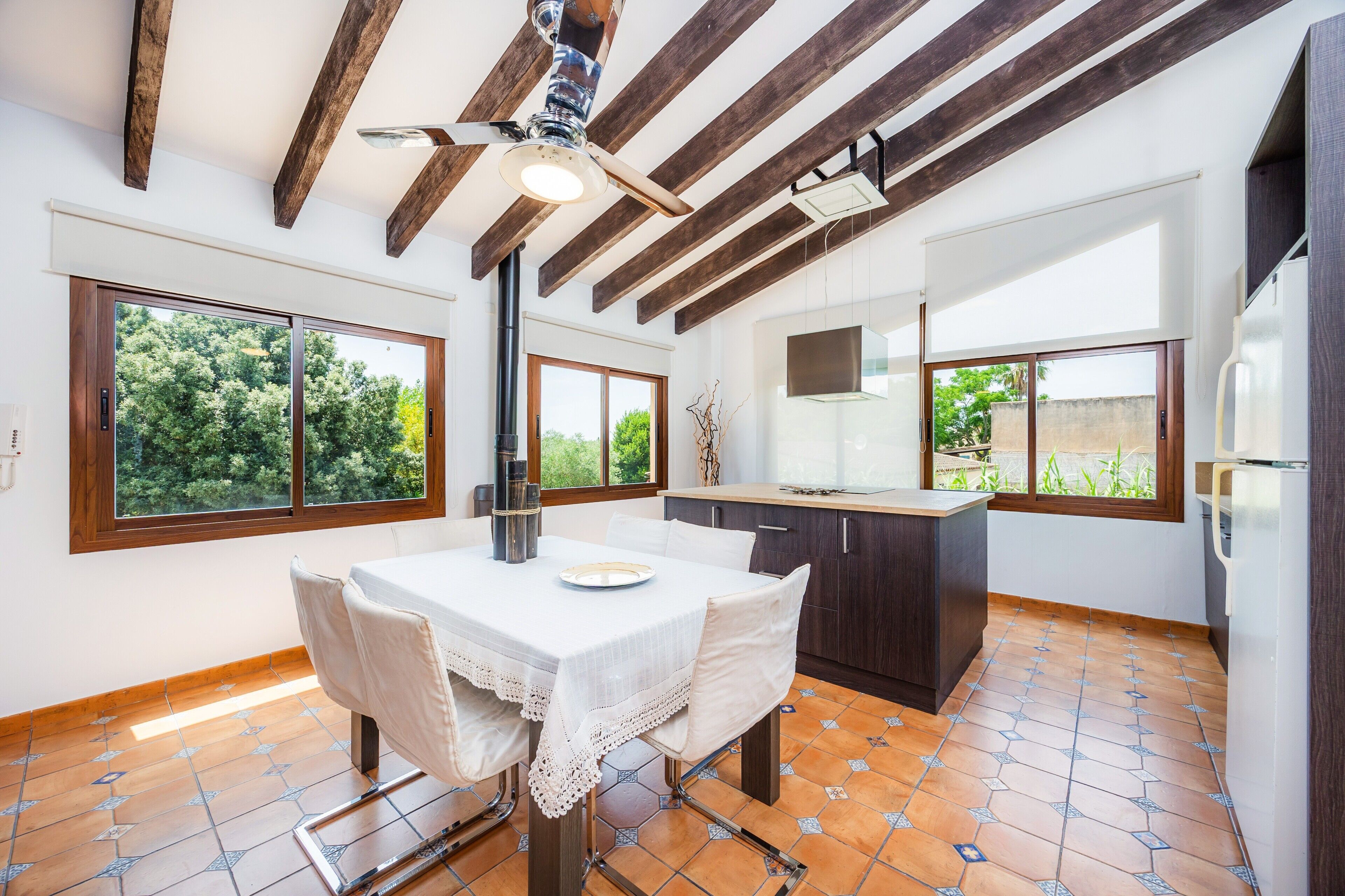 A spacious kitchen with a dining area, large windows, and a ceiling fan.