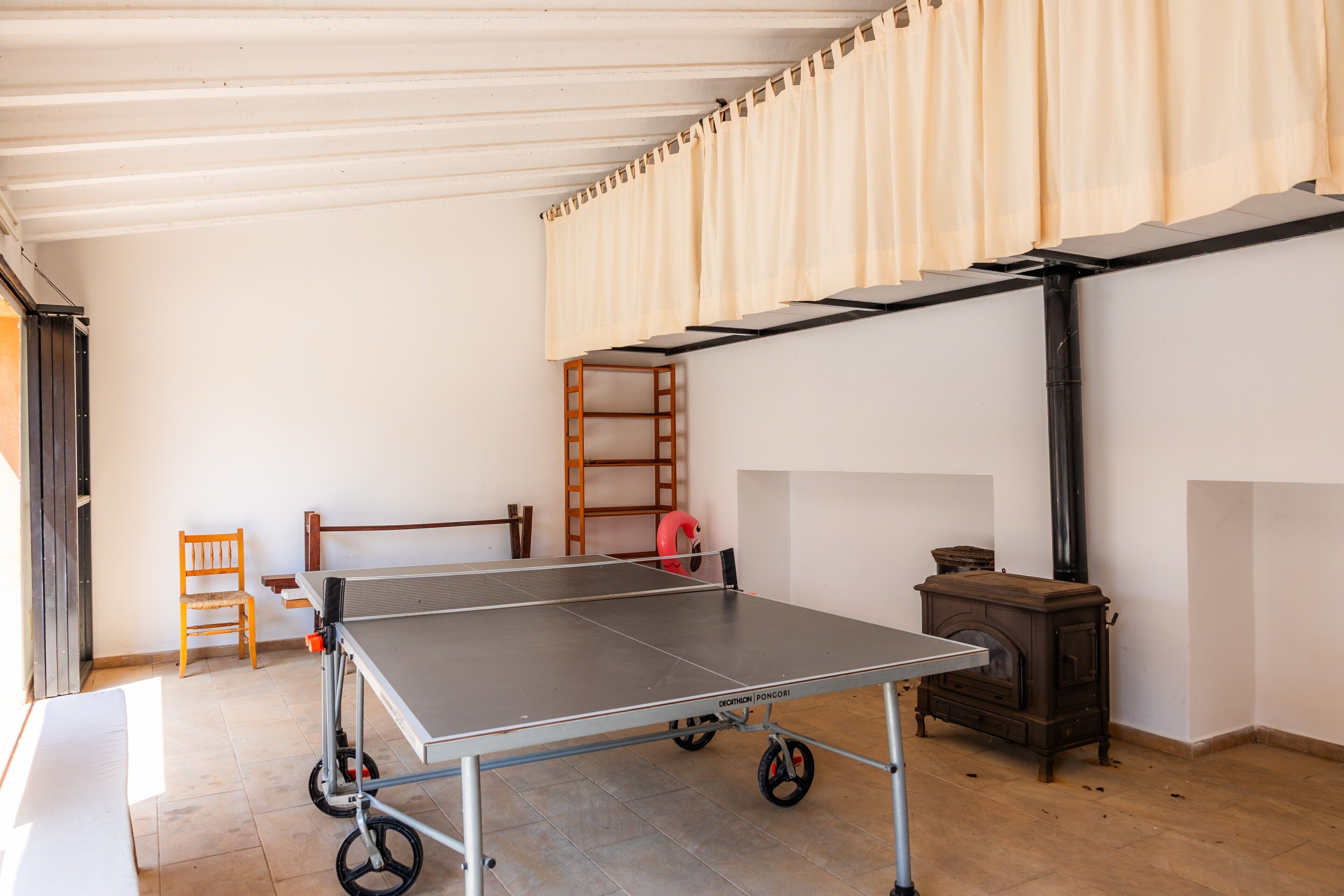 A room with a ping pong table, a wooden chair, a ladder, and a wood-burning stove.