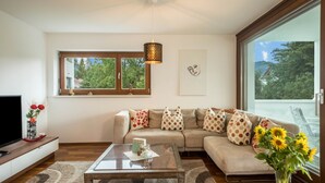 A modern living room with a sofa, a coffee table, a TV, and a large window with a view of trees. - Comfortable Holiday Apartment "Felix" with Balcony, Wi-Fi & TV (Bregenz)