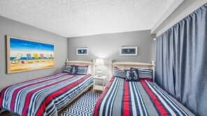 Habitación de hotel con dos camas, un cuadro con motivos playeros y dos fotografías enmarcadas en la pared.