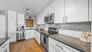Una cocina moderna con armarios blancos, electrodomésticos de acero inoxidable y suelo de madera.