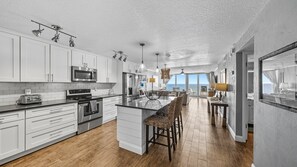 Una cocina moderna con armarios blancos, electrodomésticos de acero inoxidable y una isla central con taburetes de bar.
