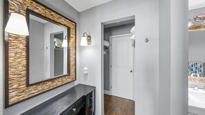 A modern bathroom with a large mirror, wall-mounted lights, and a wooden accent wall. - Coastal Luxury - Shores Club Unit 604 (Daytona Beach Shores)