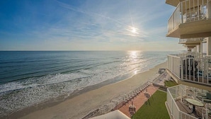 Een strandhotel met een balkon met uitzicht op de oceaan, een terras met buitenmeubilair en een helder uitzicht op de zonsondergang.