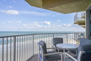 A balcony with a view of the beach, a round table, and striped chairs. - #803 Shores Club Oceanfront Traffic Free Beach 2/2 (Daytona Beach Shores)