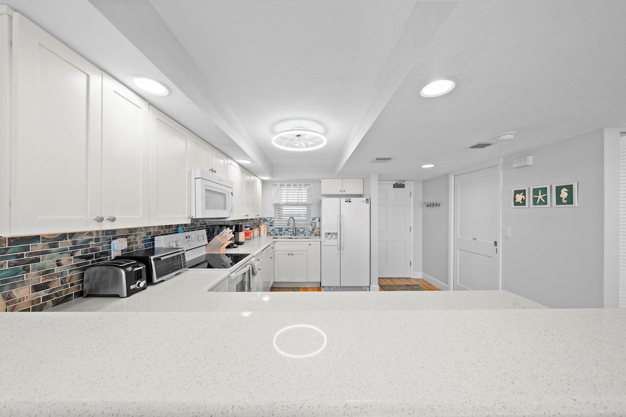 A modern kitchen with white cabinets, a tiled backsplash, and a granite countertop.