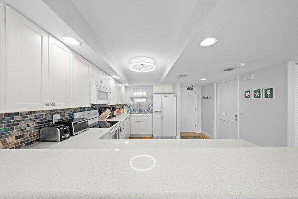 Una cocina moderna con armarios blancos, salpicadero de azulejos y encimera de granito.