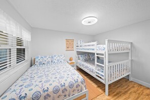 Un dormitorio con una cama litera, una cama individual y una ventana con persianas.