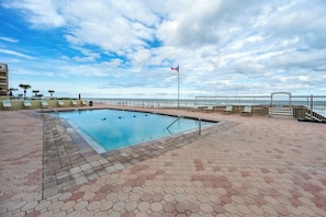 A swimming pool with a view of the ocean, surrounded by lounge chairs and a fence. - #803 Shores Club Oceanfront Traffic Free Beach 2/2 (Daytona Beach Shores)