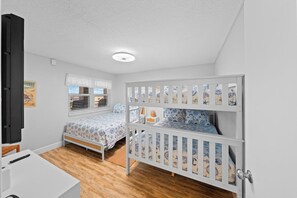 Ein Schlafzimmer mit zwei Betten, einem weißen Schreibtisch und einem Fenster mit Jalousien.