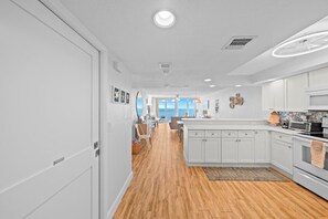 A modern kitchen with white cabinetry, a wooden floor, and a view to the outside.