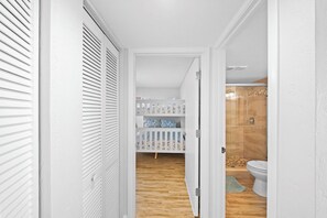 Ein Flur, der zu einem Badezimmer mit Holzboden, Toilette in Weiß und einer Duschkabine führt.