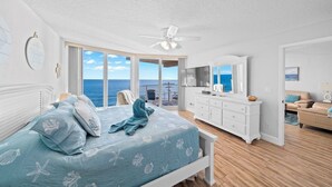 Een slaapkamer met een bed, een dressoir, een plafondventilator en uitzicht op de oceaan.