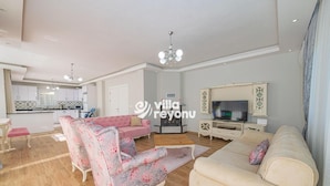 Een ruime woonkamer met een bank, fauteuils, een televisie en een eethoek met een tafel en stoelen.