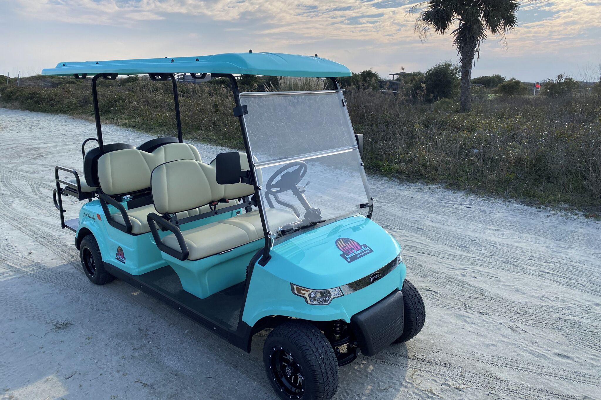 A golf cart parked on a sandy path with a clear sky.