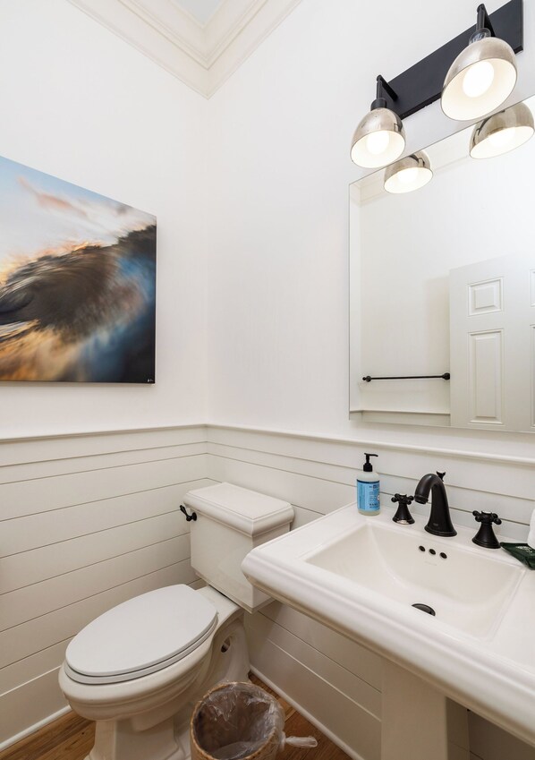 Un baño con inodoro blanco, lavamanos con grifo negro y espejo sobre el lavamanos.
