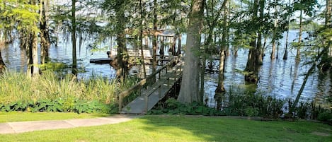 A wooden deck leading to a dock over water, surrounded by trees and grassy areas.