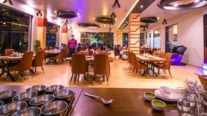 A restaurant with multiple dining tables and chairs, a variety of dishes on the tables, and hanging pendant lights.