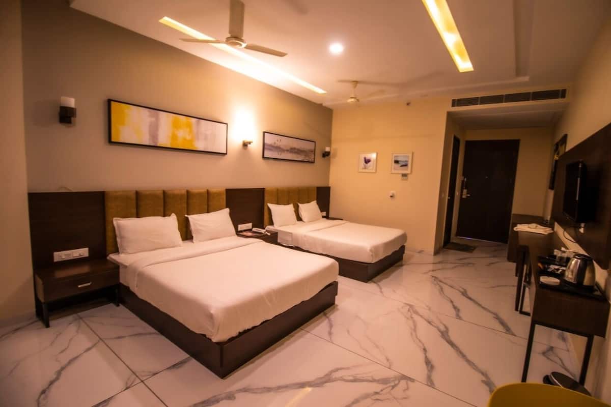 A hotel room with two beds, a ceiling fan, wall-mounted artwork, a television, and a small table with a kettle.