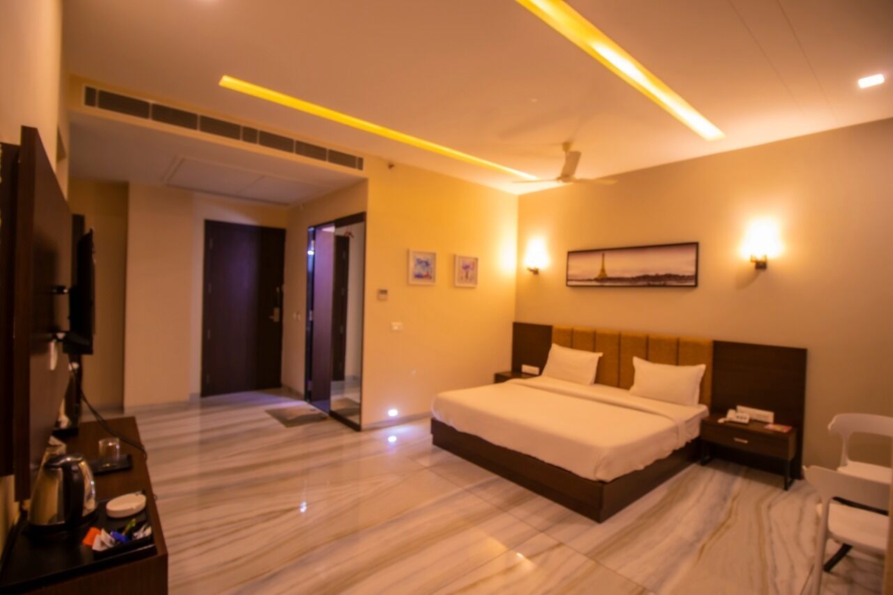 A hotel room with a large bed, bedside tables, a desk with a lamp, and a chair.