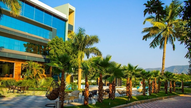 A modern building with a glass facade, surrounded by palm trees and outdoor seating areas.