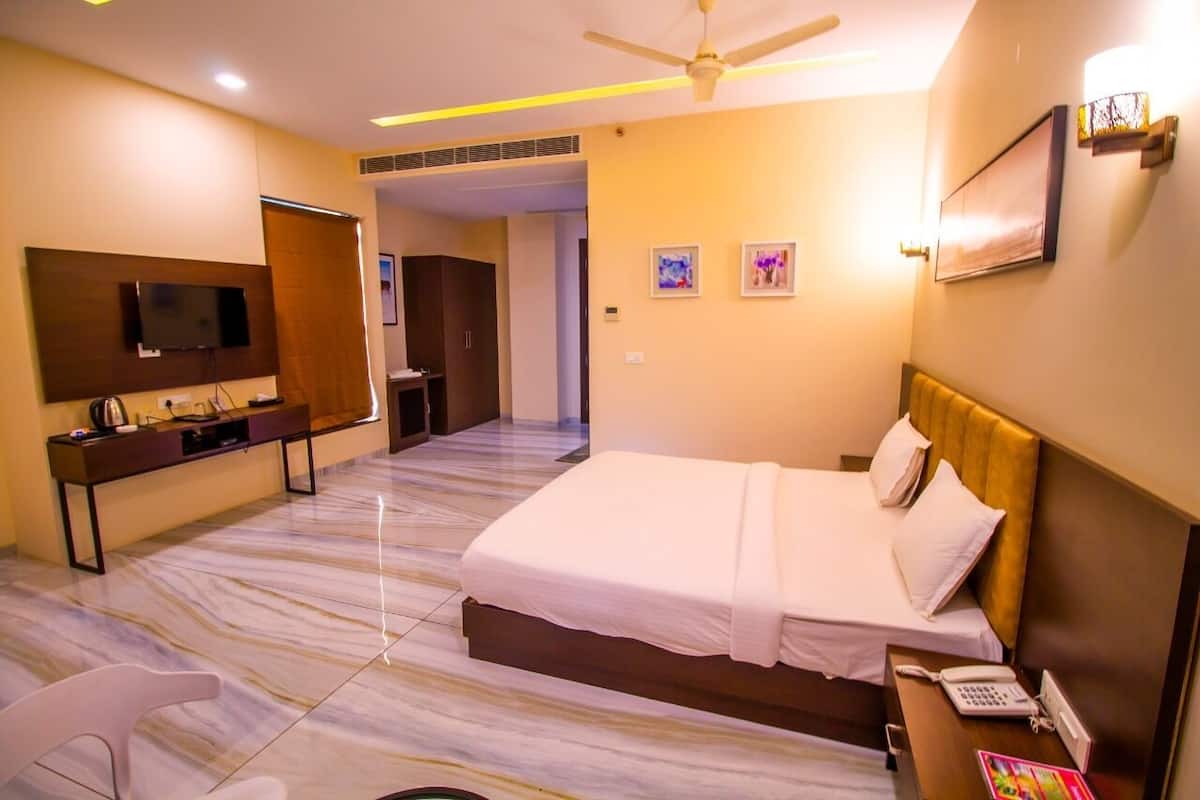 A hotel room with a bed, a desk, a chair, a television, and a ceiling fan.