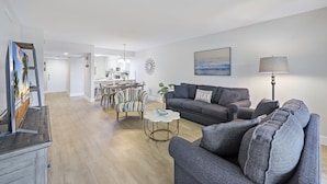 A modern living room with a grey sofa, a round coffee table, and a dining area with striped chairs. - Spacious Condo | Lanai, Pool and Steps to Beach (Marco Island)