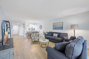 A modern living room with a grey sofa, a round coffee table, and a dining area with striped chairs.