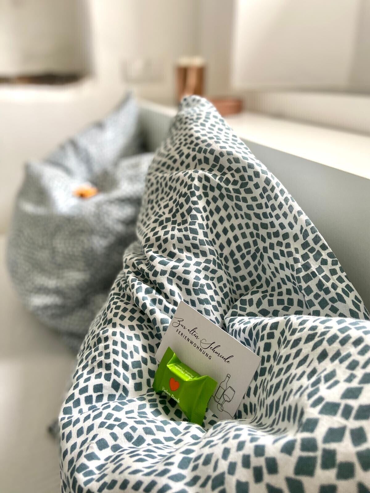 A bed with a patterned bedspread and a green gift bag with a card.