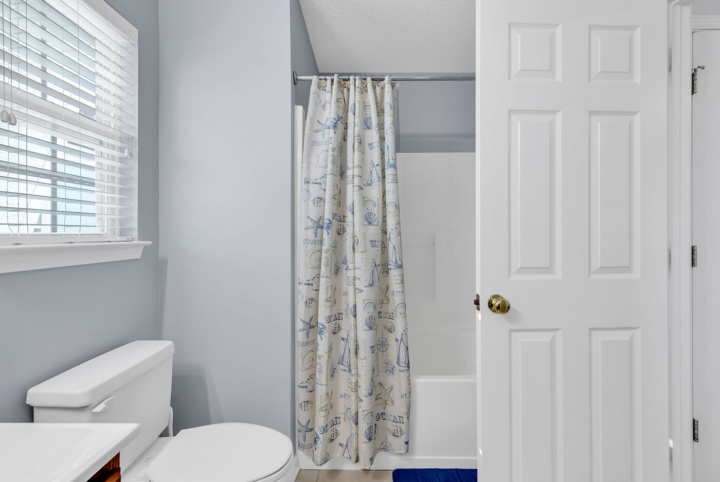 Une salle de bain avec des toilettes, un rideau de douche orné de motifs marins et une porte blanche.