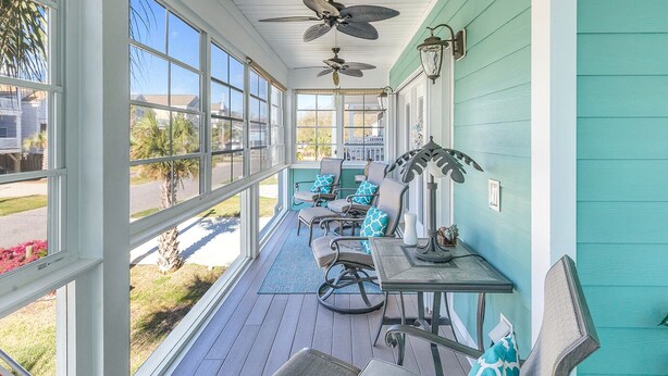 A covered porch with a ceiling fan, outdoor seating, and large windows overlooking a residential area. - Beautiful beach home! Private pool! Dates in August have been discounted! (Surfside Beach)