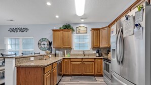 A modern kitchen with wooden cabinets, a stainless steel refrigerator, and a clock on the wall. - Beautiful beach home! Private pool! Dates in August have been discounted! (Surfside Beach)