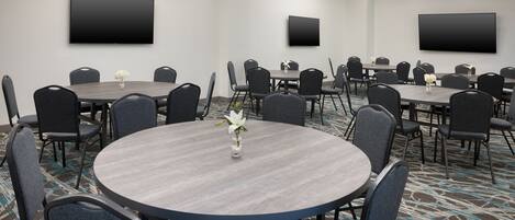 Un salón de conferencias con varias mesas y sillas, un televisor de pantalla plana en la pared y una alfombra estampada.