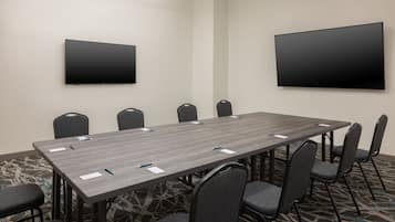 Un salón de conferencias con una larga mesa, varias sillas y dos televisores instalados en las paredes.